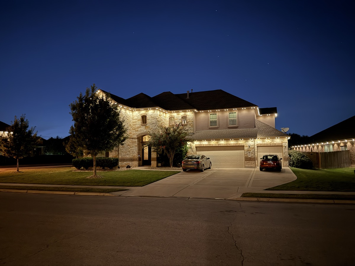 TruLight permanent warm white lighting on a two-story Austin stone home in the evening